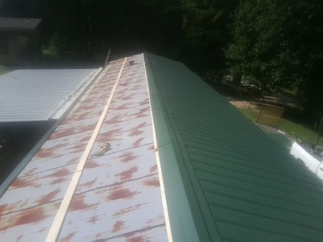 Old rusted panels beside newly installed green metal roofing — Wind Damage Roof Repair by Roofing Brothers in Onancock