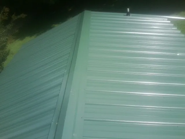 New green metal panels meeting at the ridge of a roof — Flat Roof Repair work by our crew in Onancock