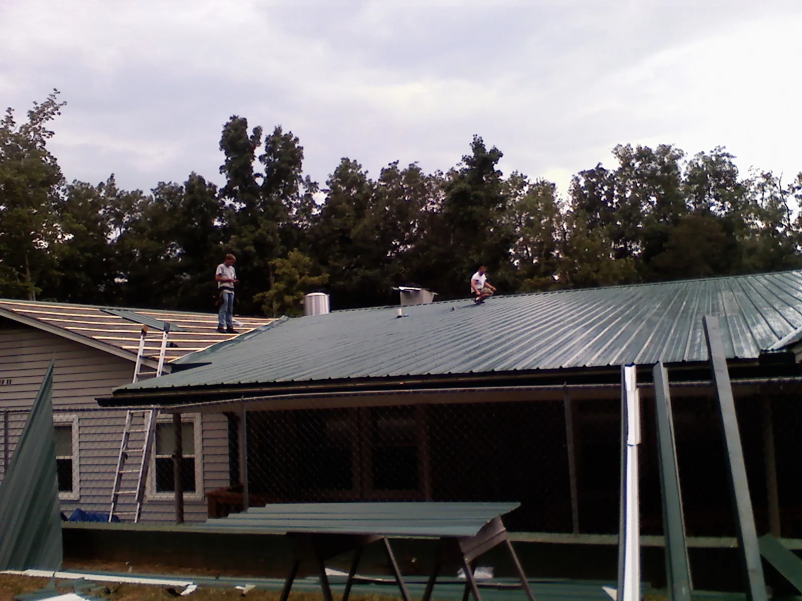 Two roofers installing green metal panels above a covered porch in Onancock