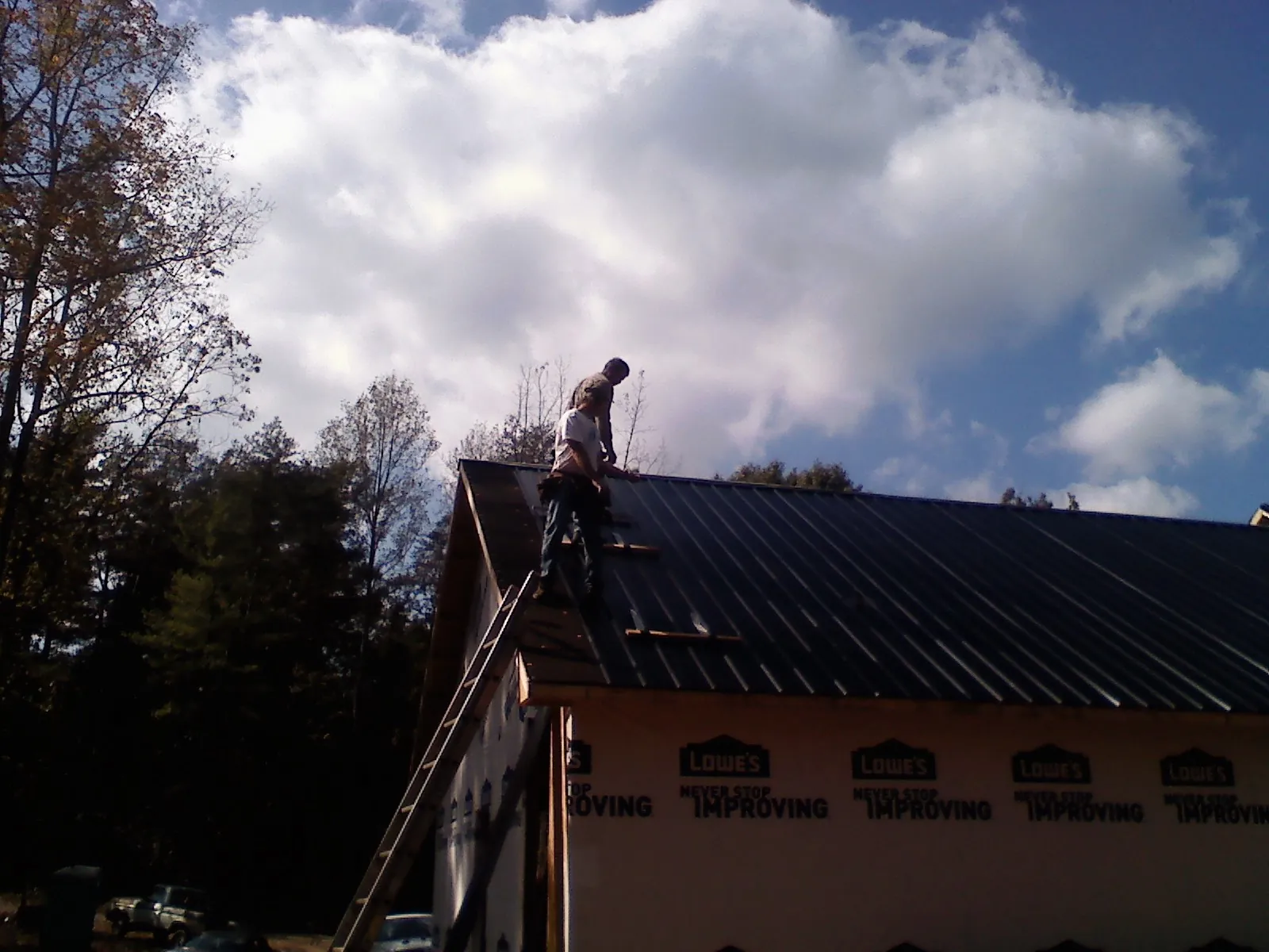 Roofer fastening dark metal panels high against a cloudy sky, from a Roof Inspection job in Onancock