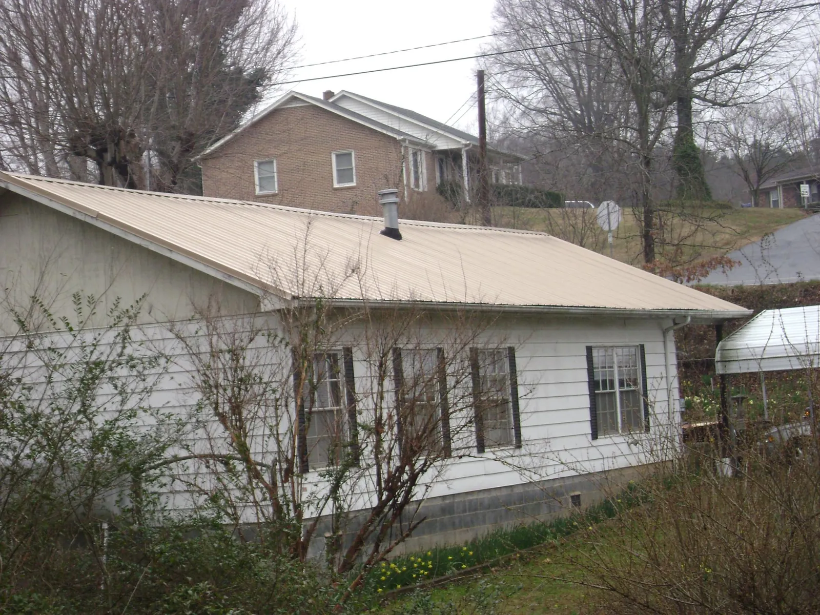 Tan metal roof on a white sided house set into a hillside — Commercial Roofing by Roofing Brothers in Onancock